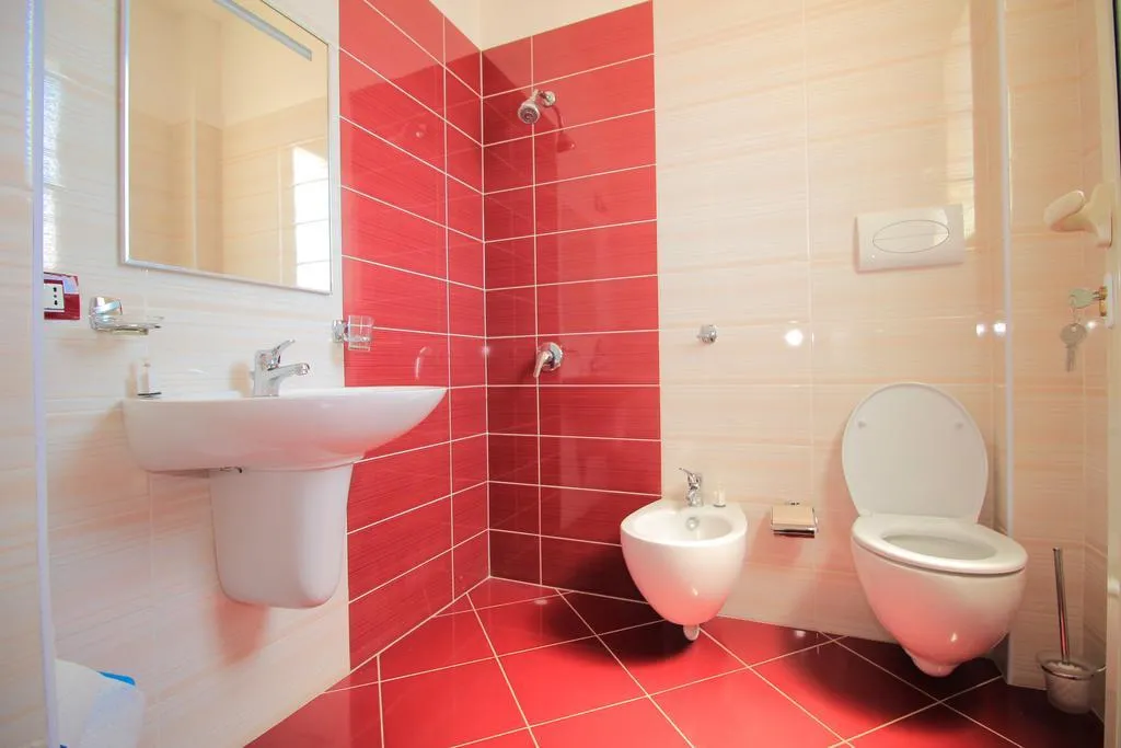 A shower room at Hotel Keisa tiled red and white, with a basin, a toilet and a bidet