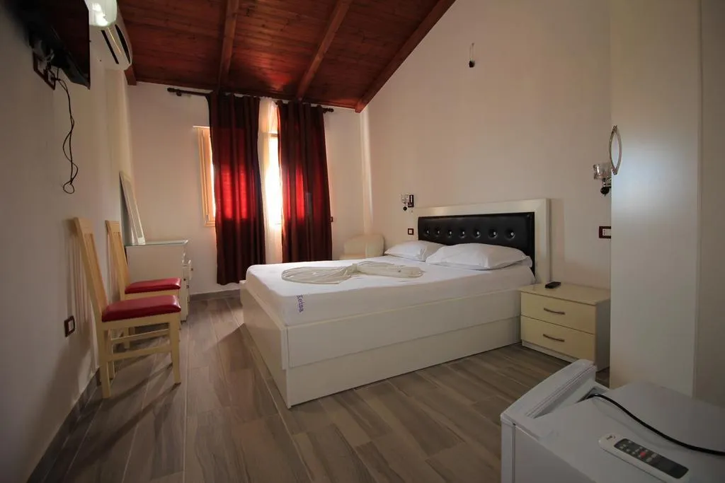 A top-floor double room at Hotel Keisa under a pitched timber ceiling, with red curtains, a white bed with a black headboard and two wooden chairs