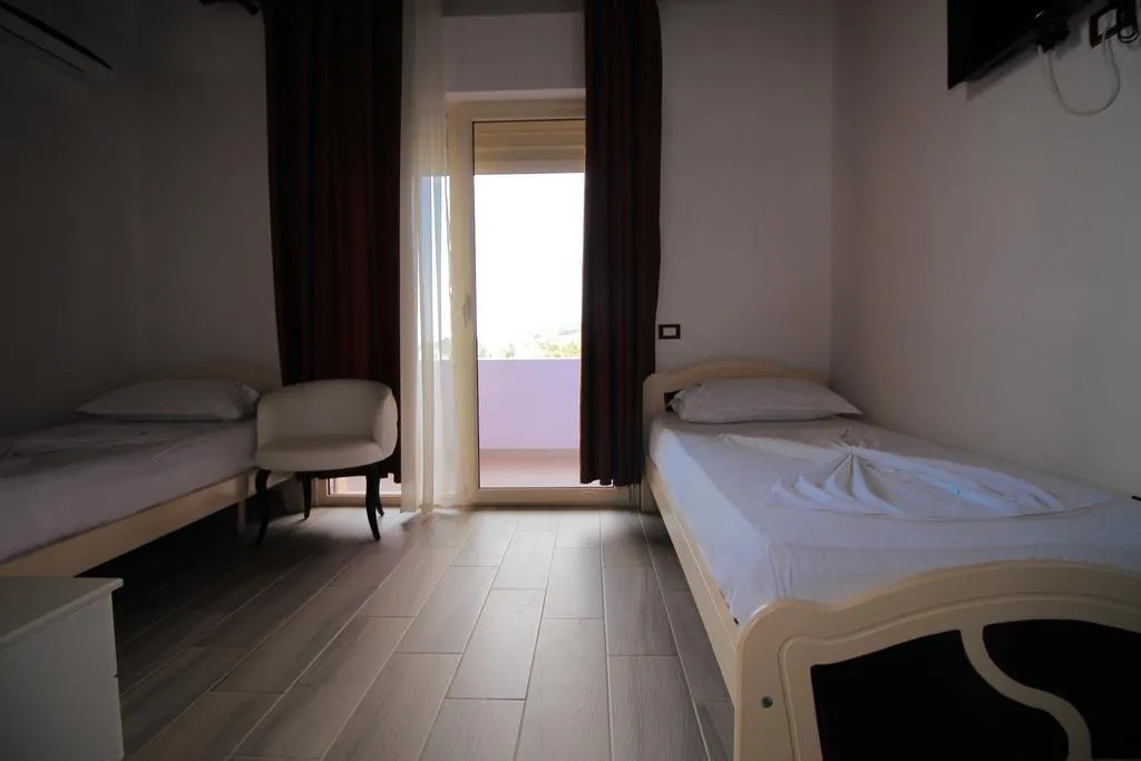 A twin room at Hotel Keisa with a white chair between the beds and the balcony door open to the light