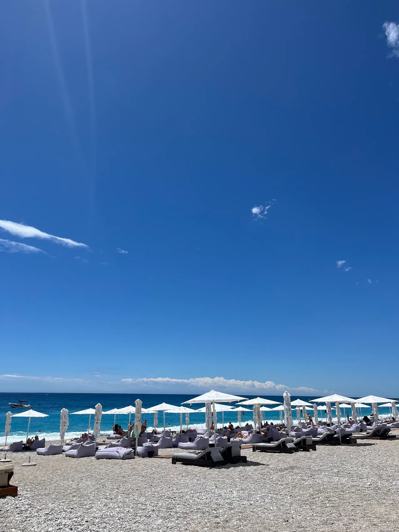 White umbrellas and loungers on the pale pebbles of Dhërmi beach under a deep blue sky, with turquoise water behind