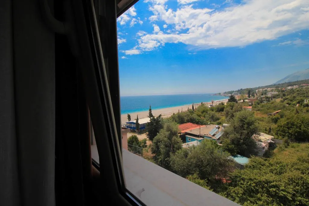 The view from a window at Hotel Keisa over olive trees and low rooftops to Dhërmi beach and the coast running north