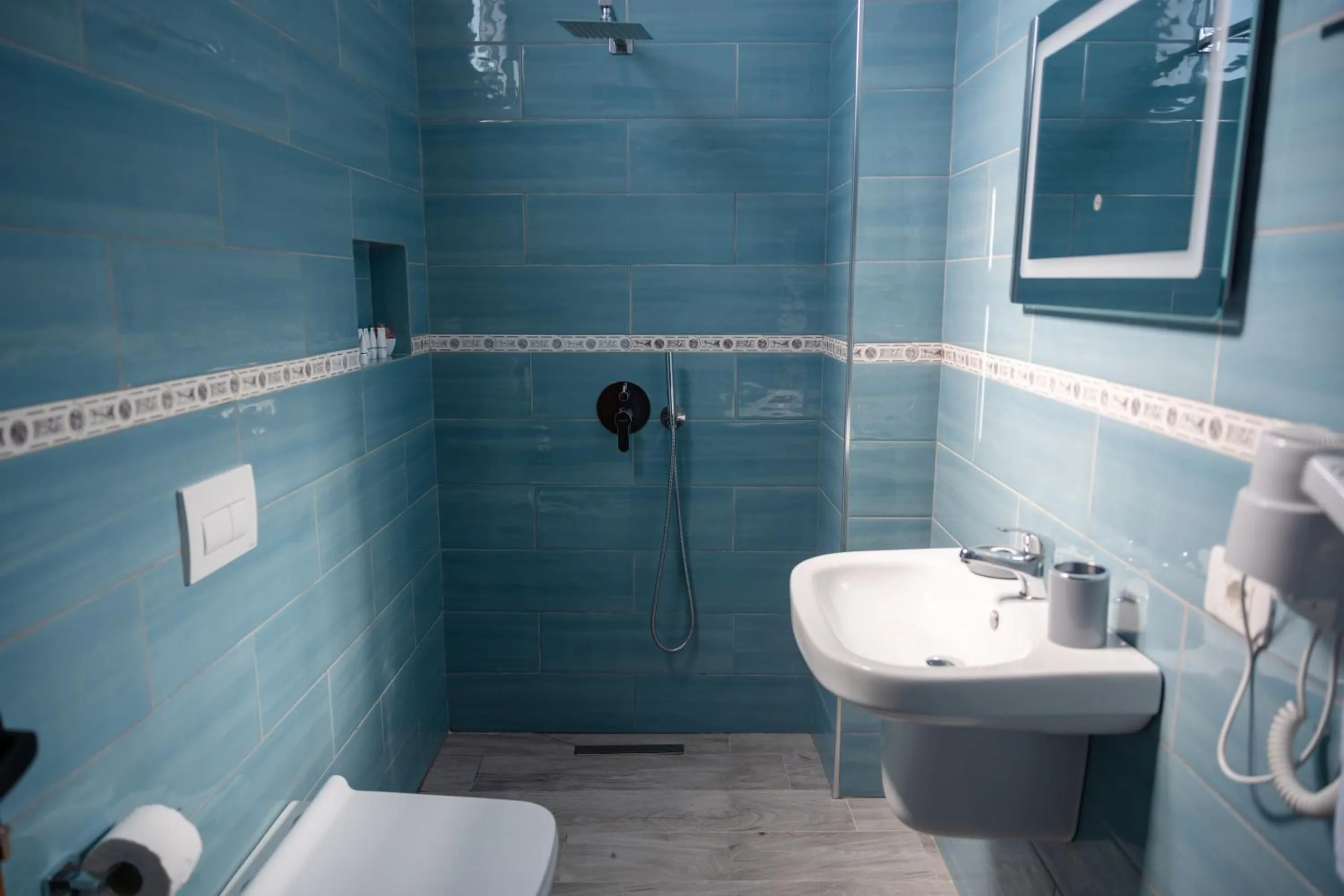 A walk-in shower room tiled in blue with a key-pattern border, a rain head and a lit mirror