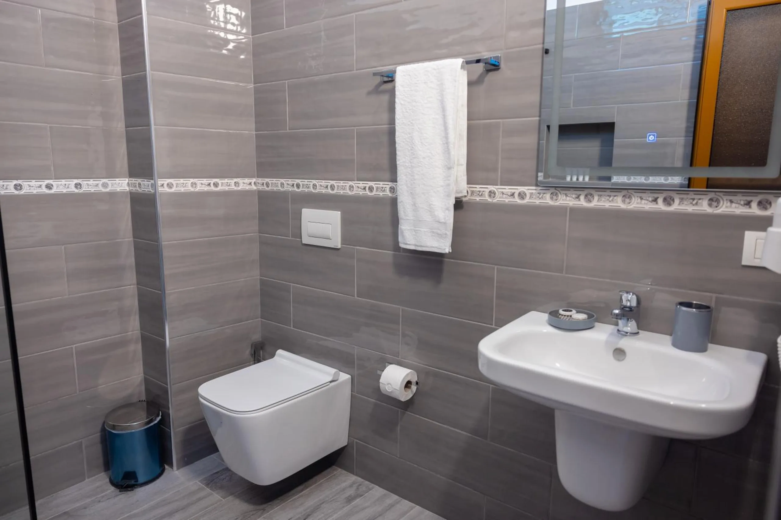 A grey-tiled shower room with a wall-hung basin and toilet and a towel rail