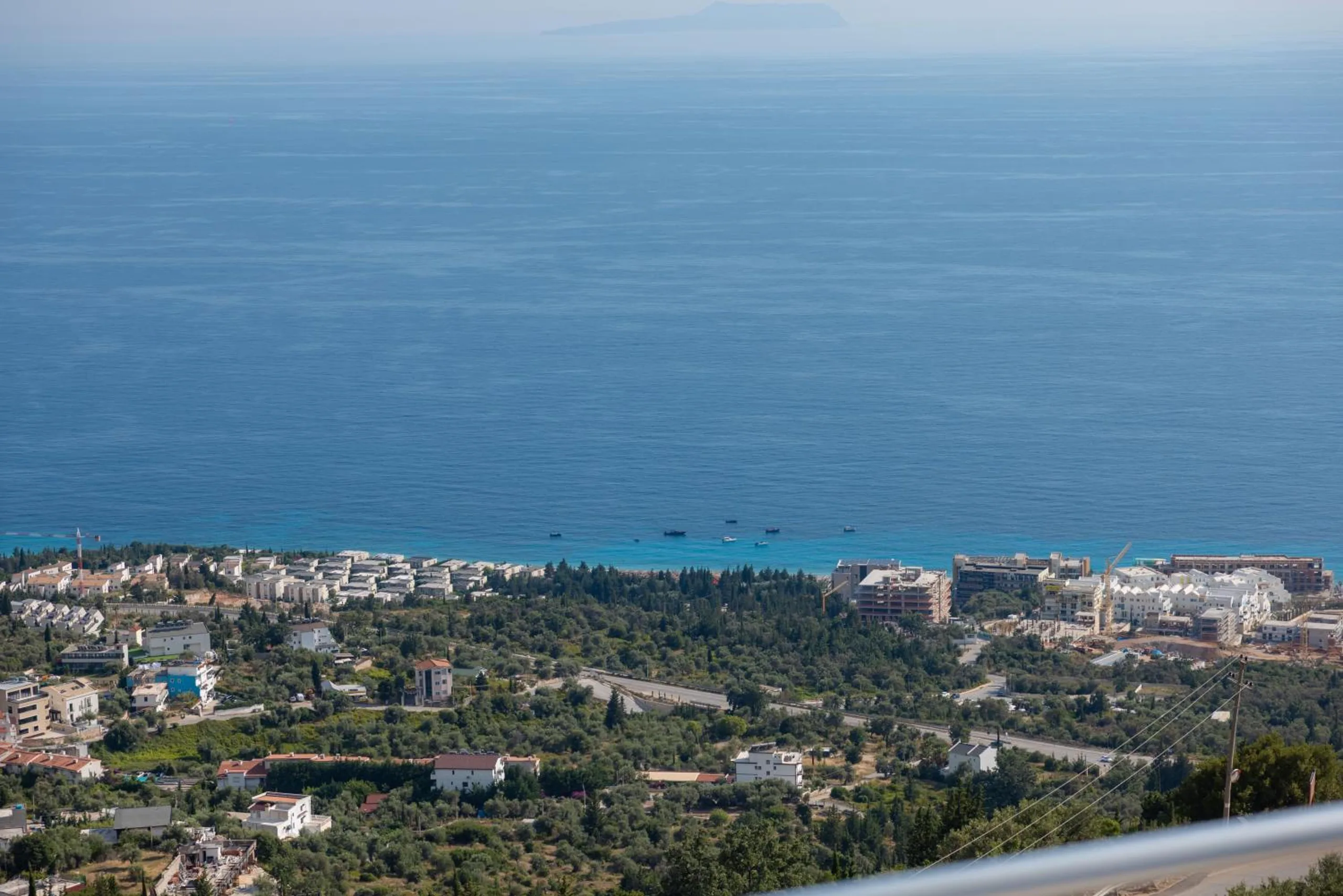 Drymades seen from the hill: houses among olive groves, the coast road and boats moored off the beach
