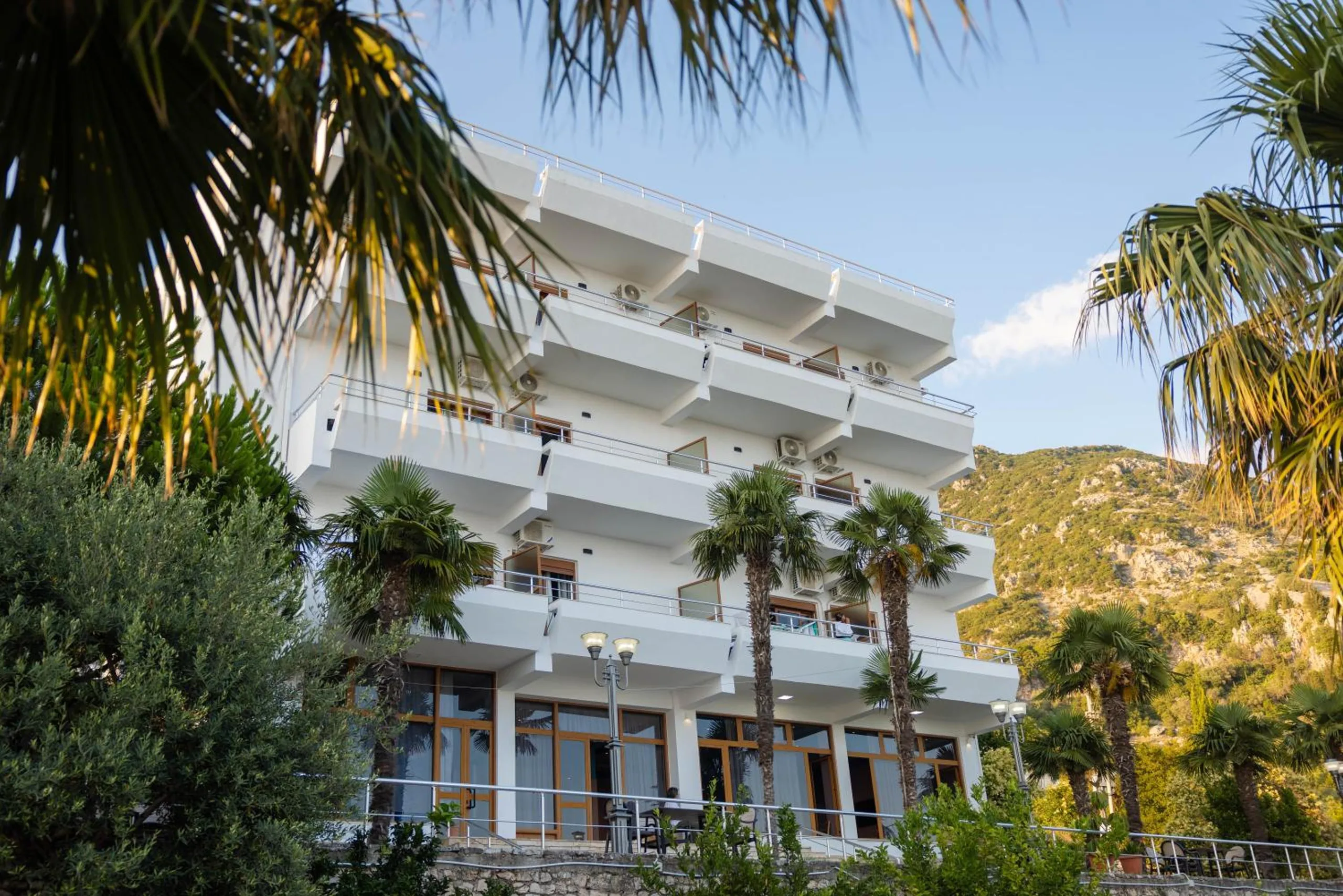 The white facade of Hotel Palasa with stacked balconies, framed by fan palms