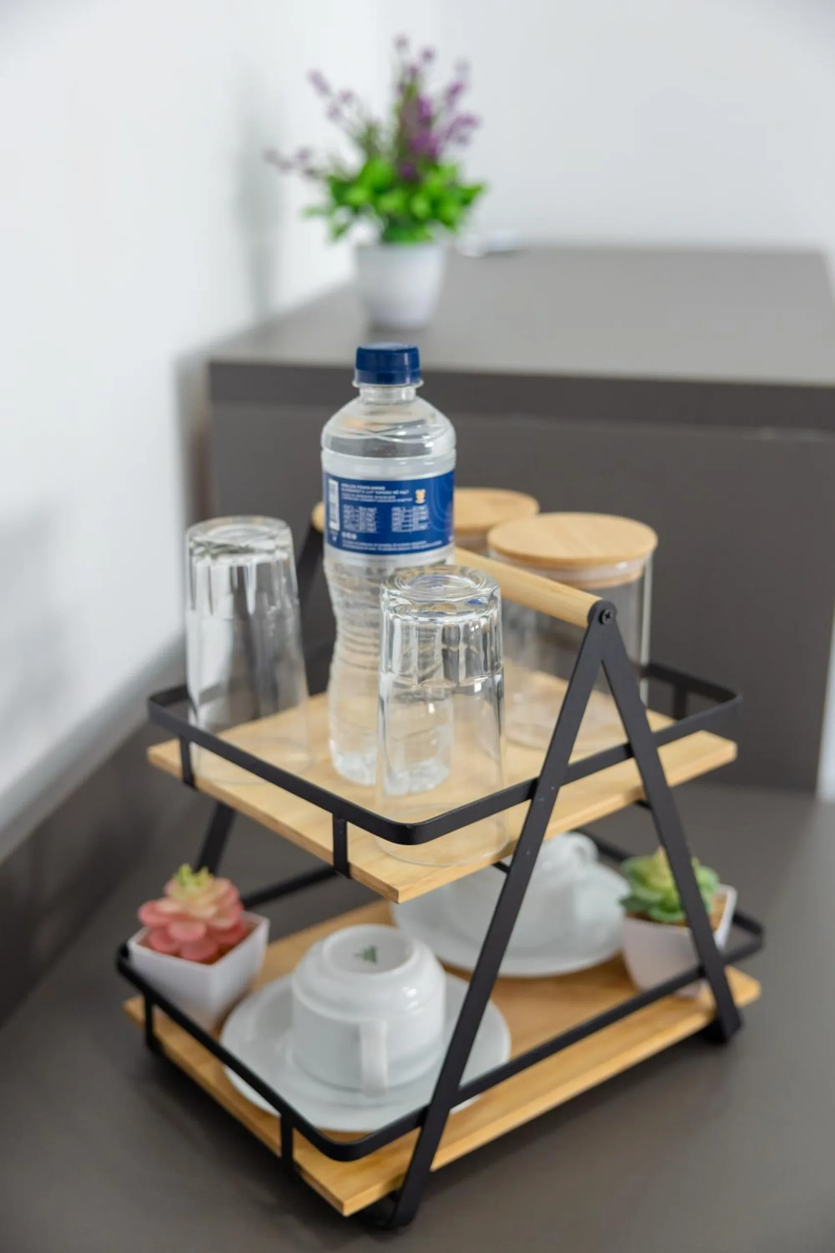 A small oak-and-steel tray stand with glasses, a bottle of water and lidded jars