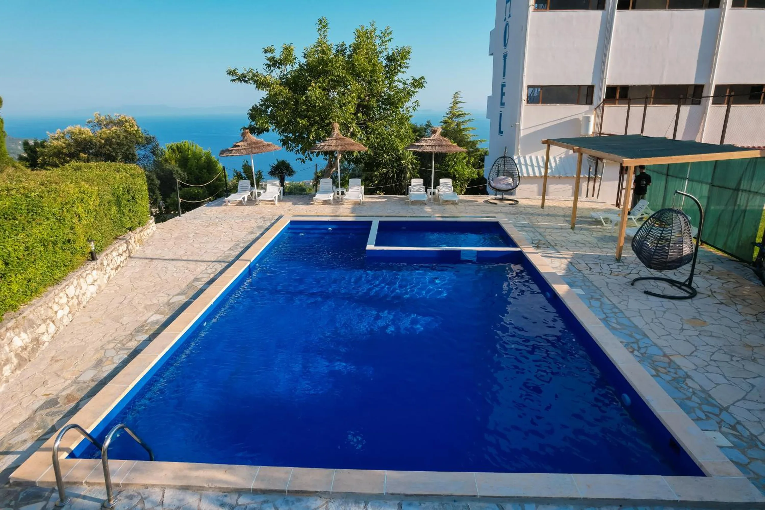 The hotel's deep-blue pool with a separate children's section, straw parasols and white loungers along the far edge