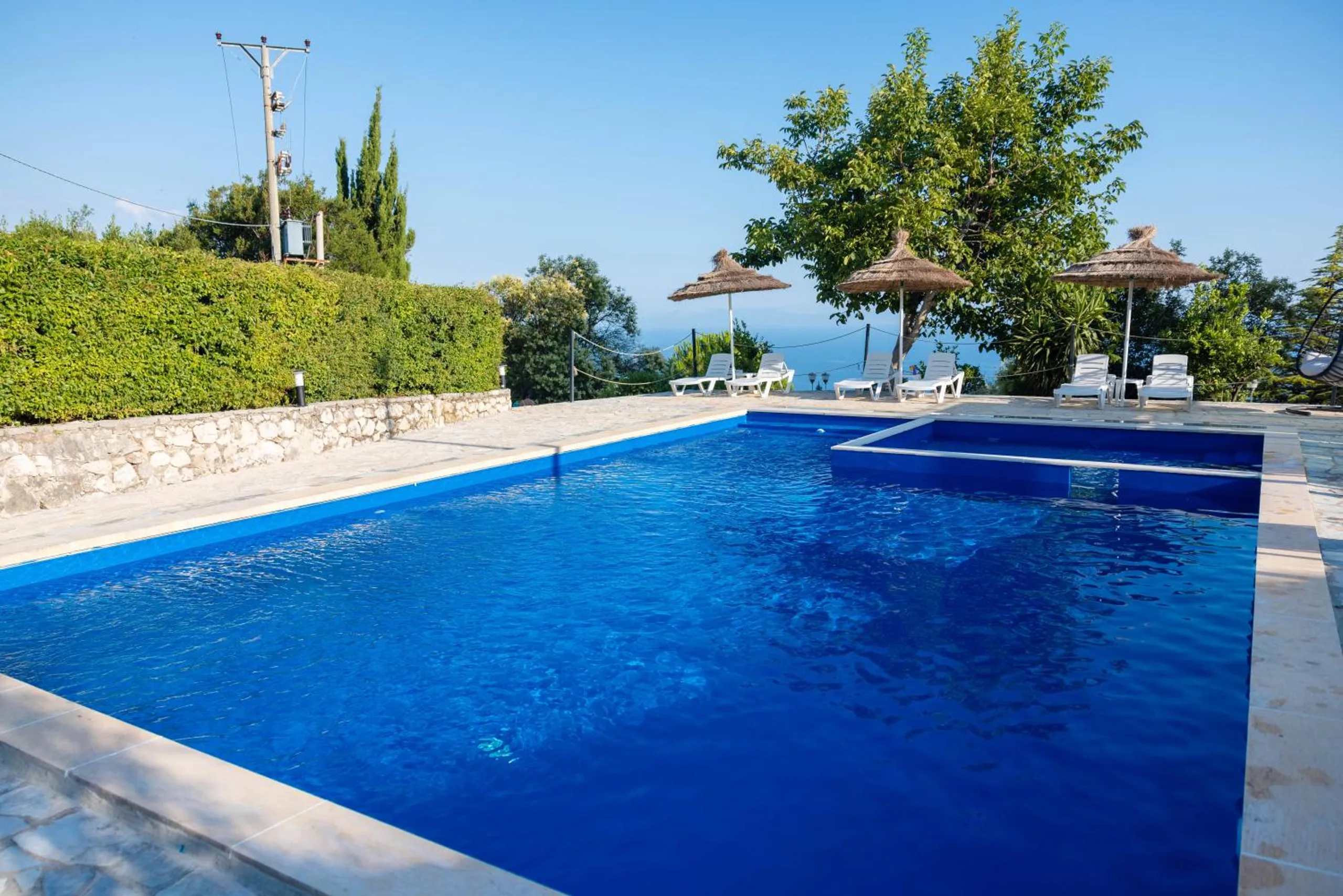 The full length of the pool with its children's section, a hedge and loungers under parasols