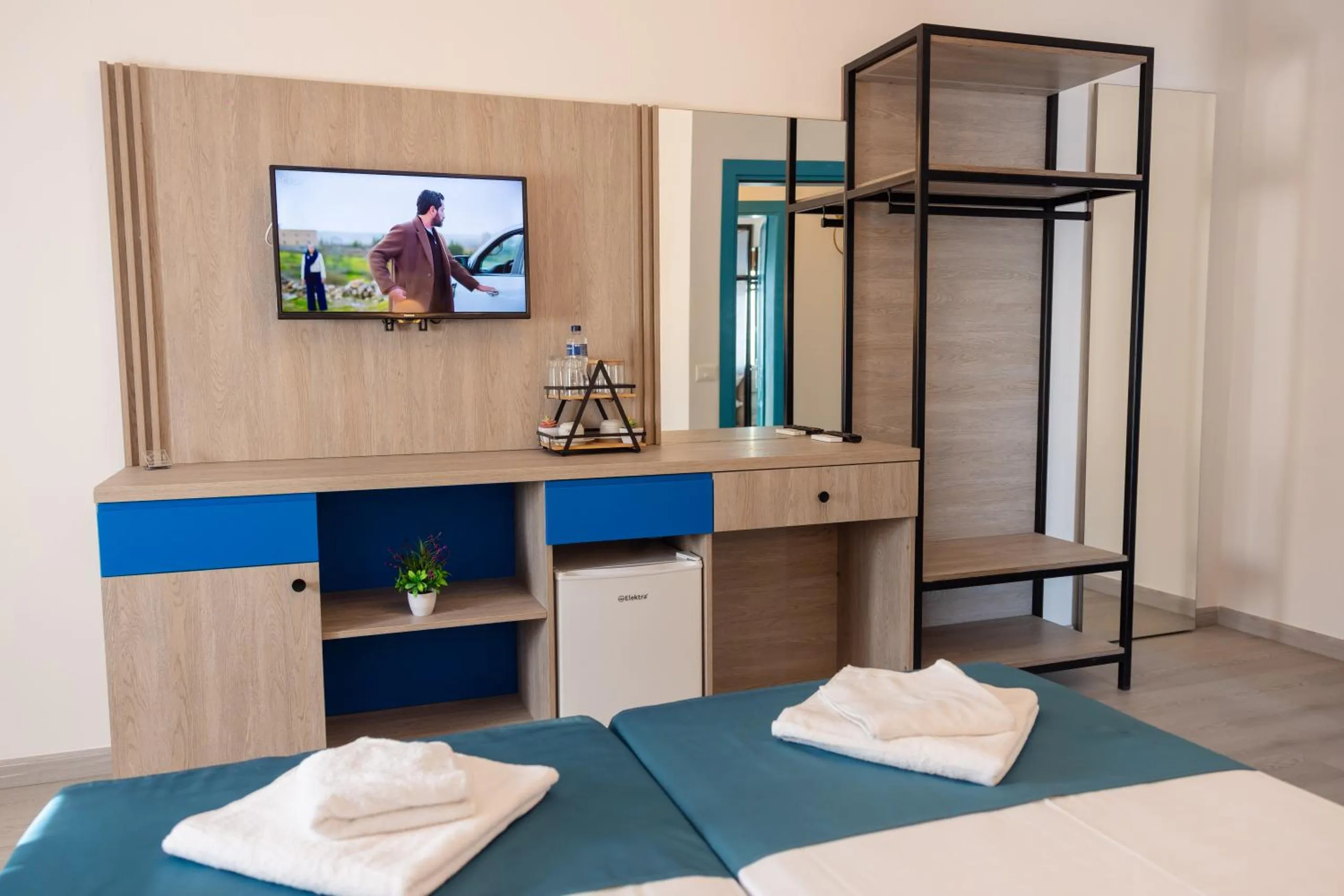 An oak-panelled desk with a wall television, a blue drawer front, a small fridge and a black steel clothes rack