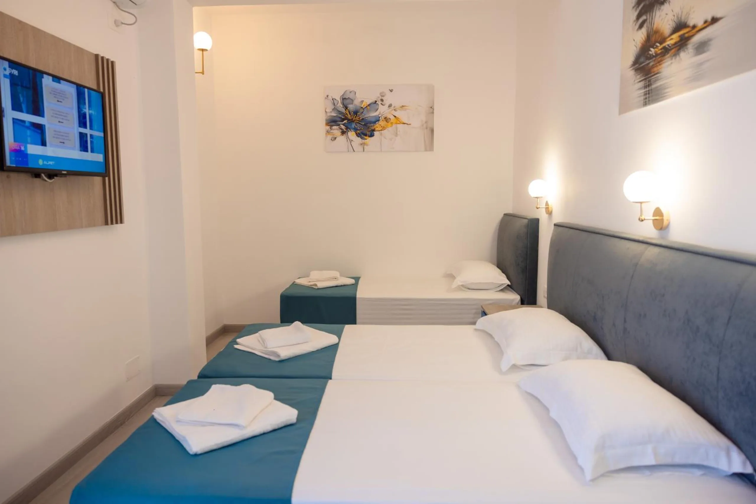 A room with a double bed and a single bed under wall lamps, blue-grey velvet headboards and teal runners