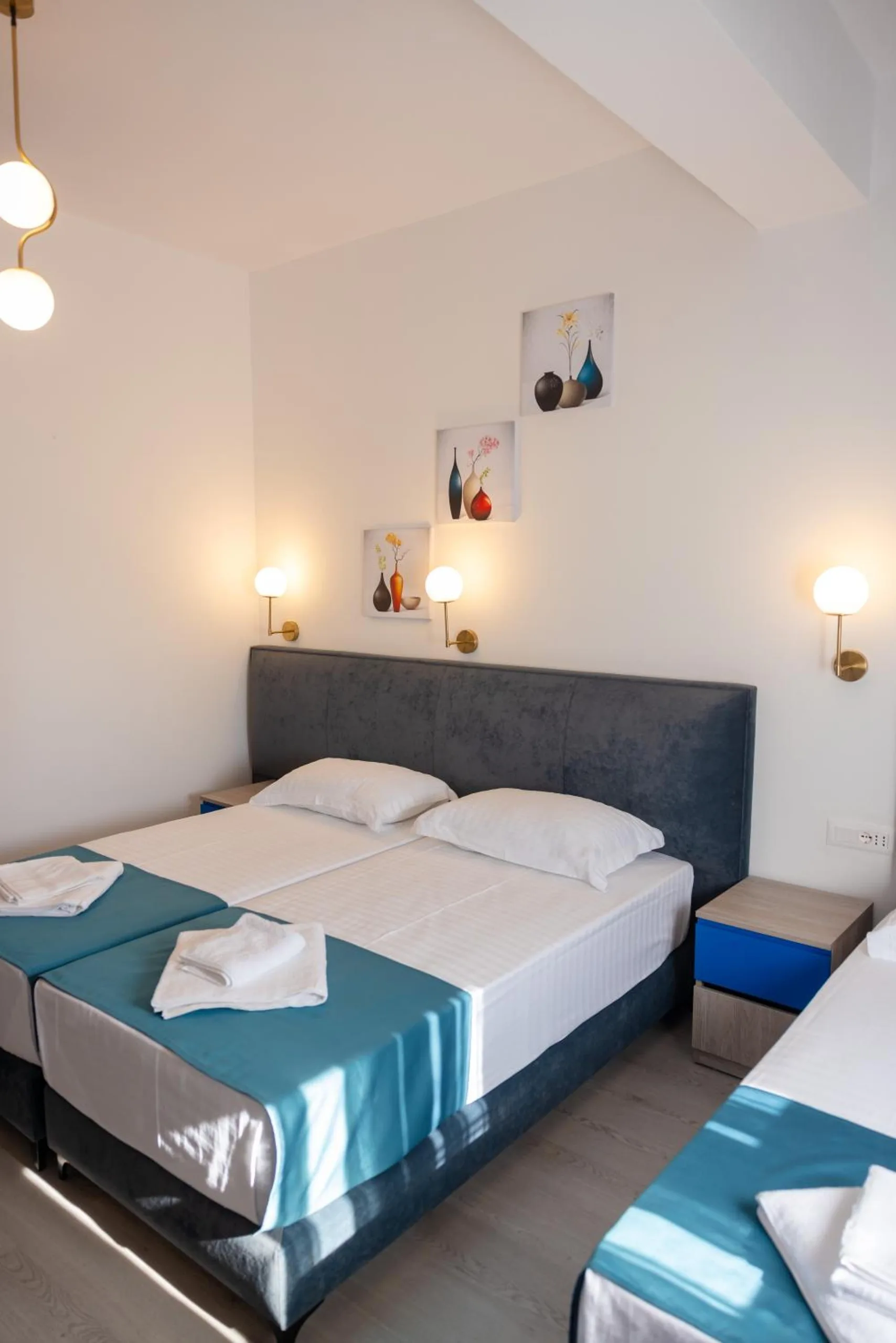 A double bed with a dark headboard between two globe wall lamps, small paintings above