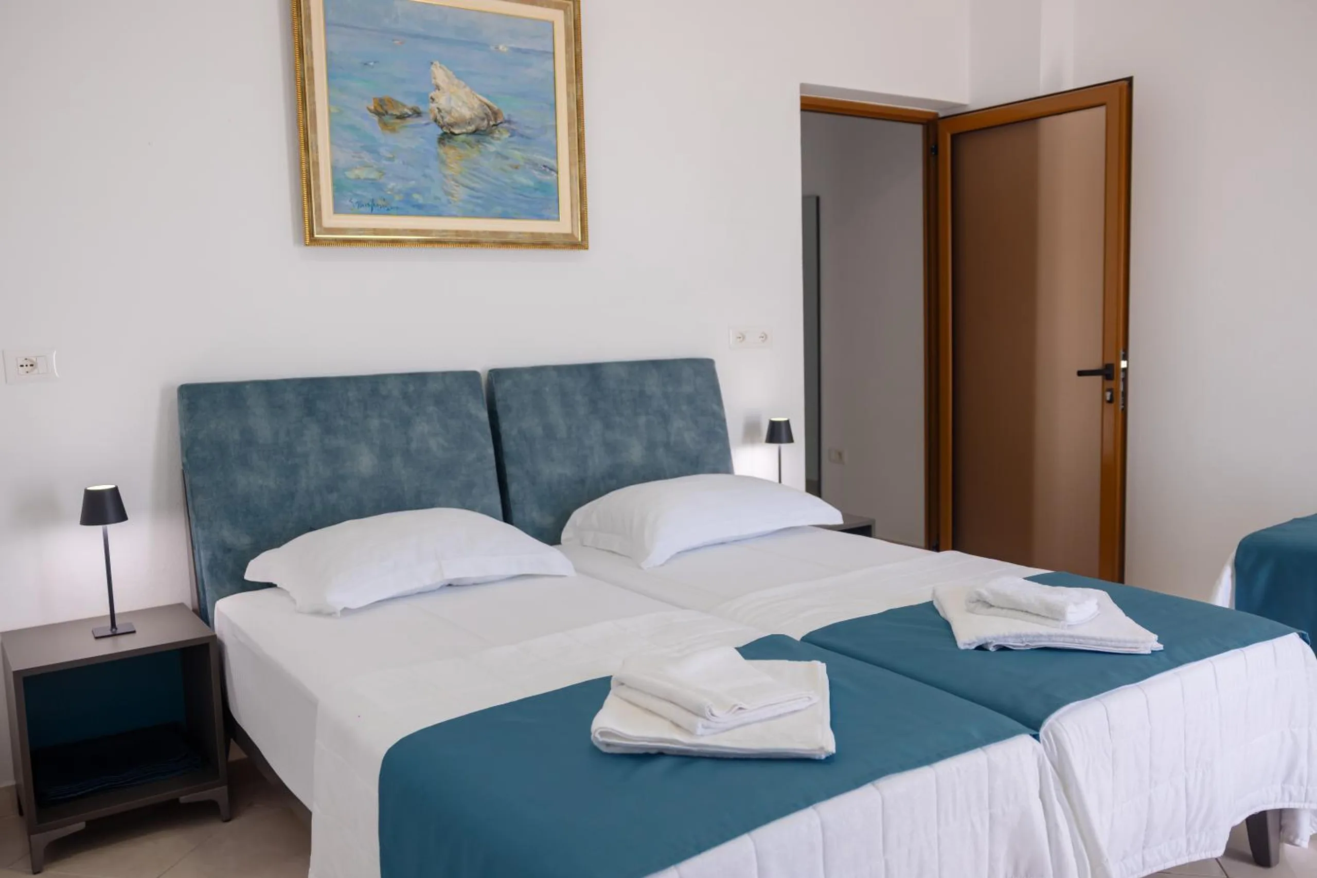 Two beds under a blue velvet headboard with a framed painting of a turtle on a rock above