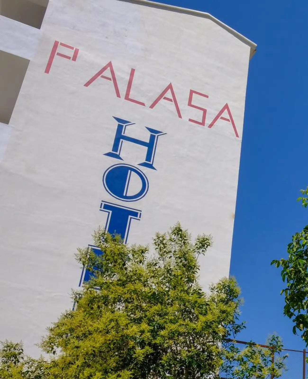 The gable of the hotel with PALASA painted in thin rose capitals over a vertical HOTEL in blue
