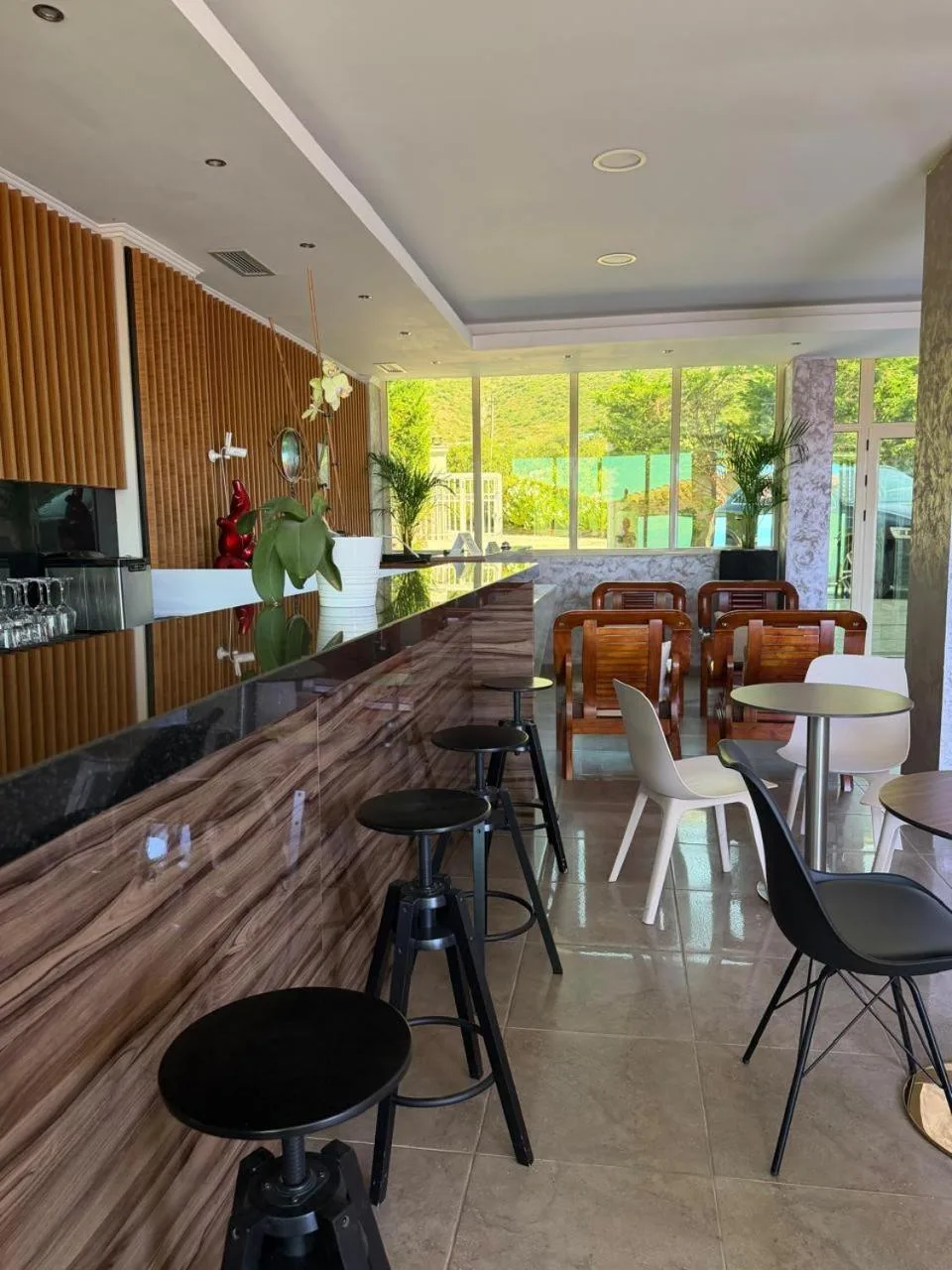 A timber bar counter with high stools and a slatted wall, the garden visible through glass at the far end