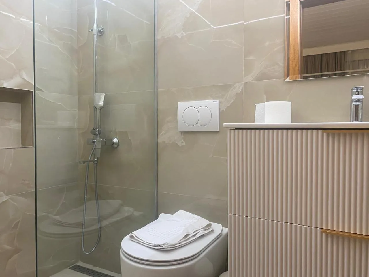 A marble-tiled shower with a glass screen, a wall-hung toilet and a ribbed vanity unit