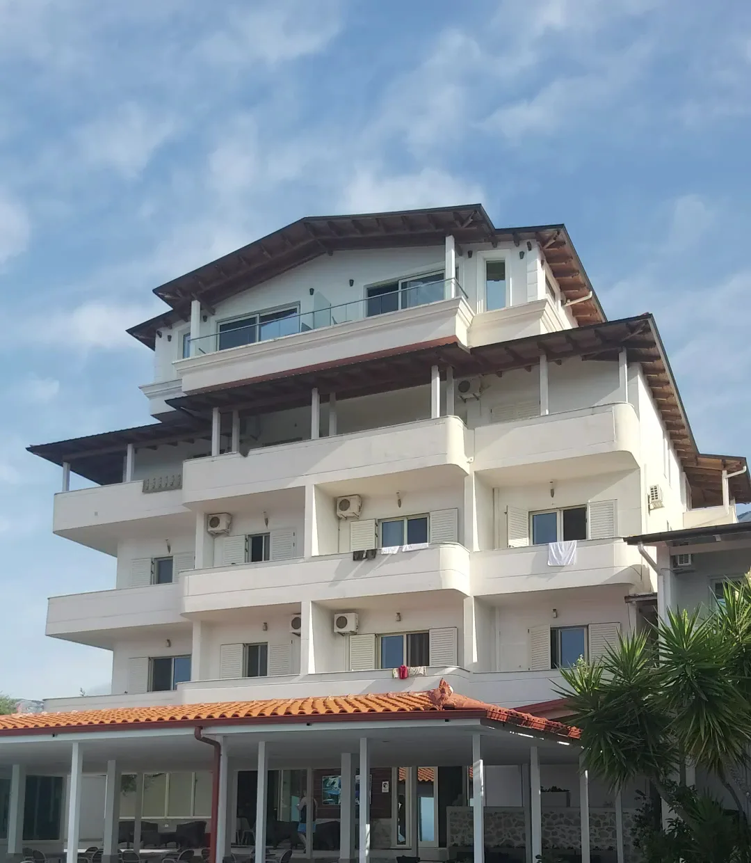 The white five-storey hotel with stacked balconies and pitched timber roofs, above a single-storey pavilion with an orange tile roof