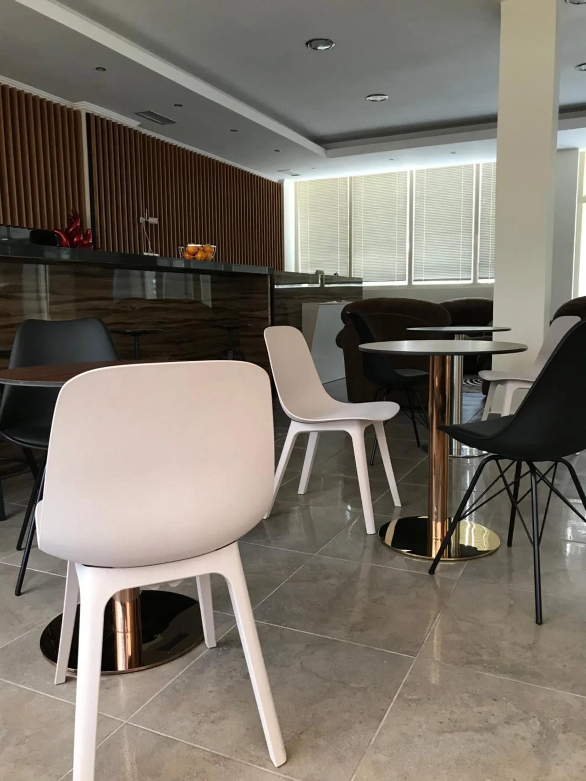 White and black chairs around small round tables in the hotel's café area, with a slatted wall behind