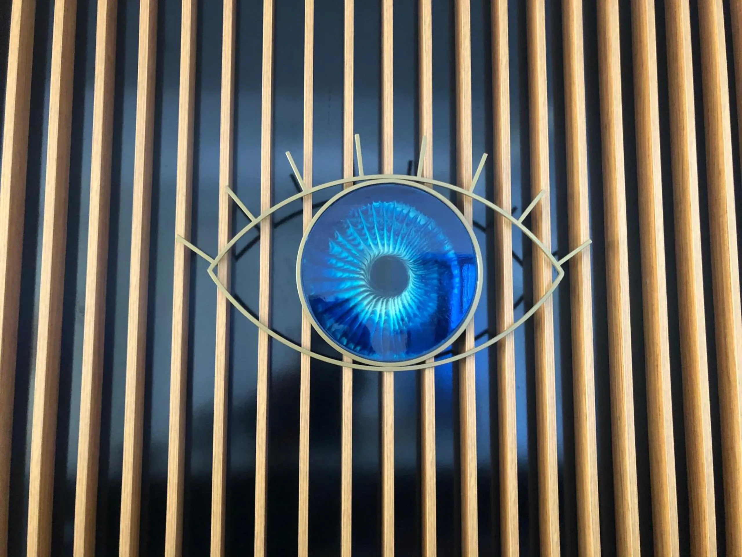 A blue glass evil eye in a brass frame mounted on a wall of vertical timber slats