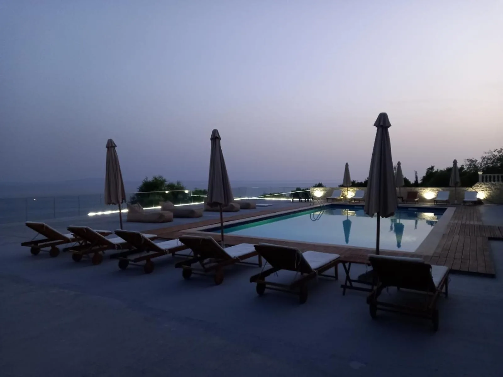 Loungers lined up on the pool deck at dusk with the sea fading into haze