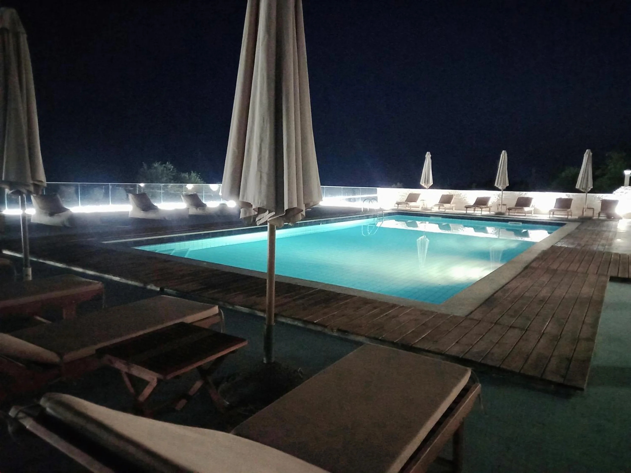 The pool lit turquoise at night, loungers in the foreground and a lit glass balustrade along the far edge