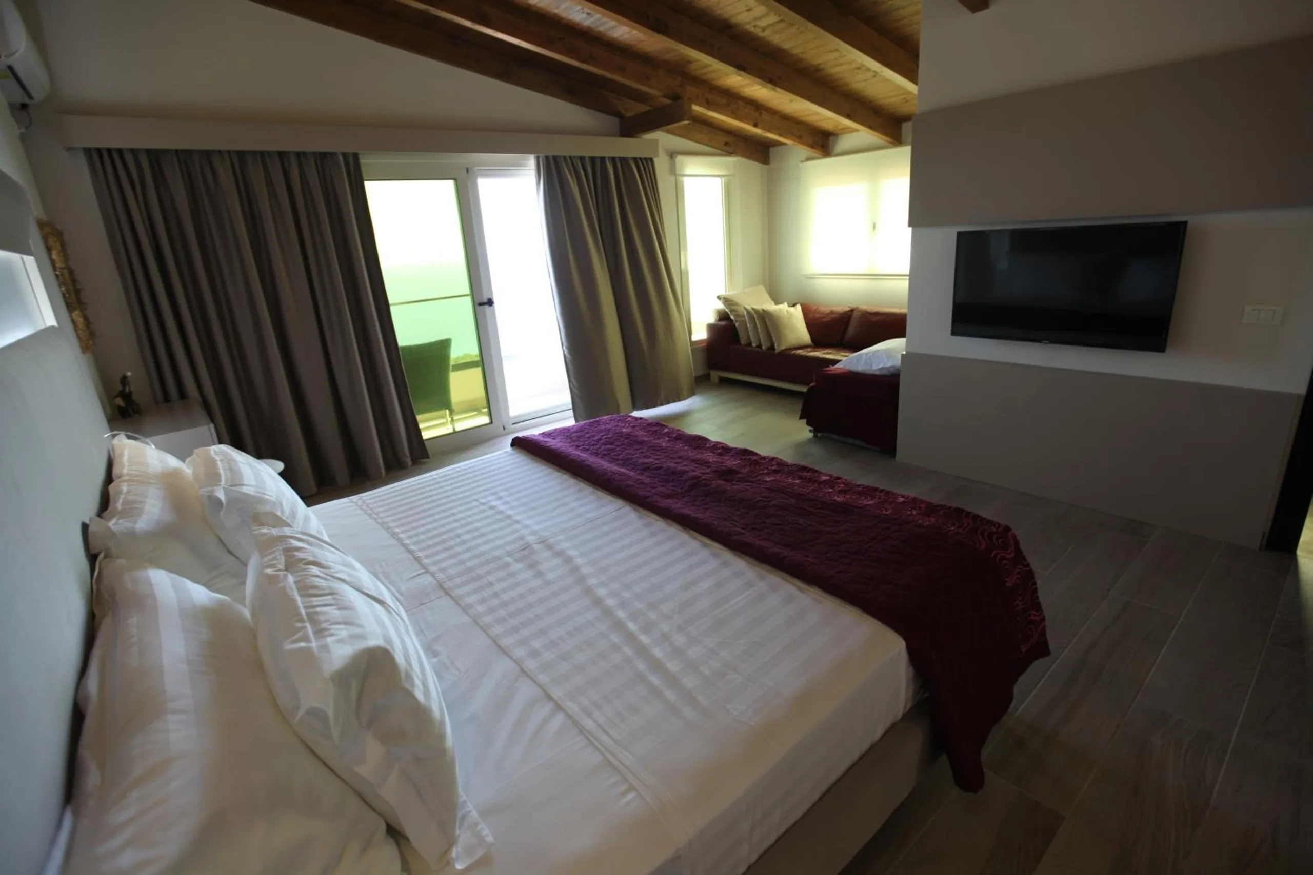 The suite's double bed with a burgundy runner, a TV and a sofa by the balcony doors