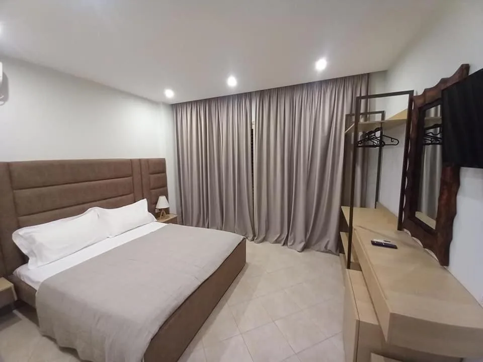 A double bed with a brown padded headboard, long grey curtains and an open wardrobe rail