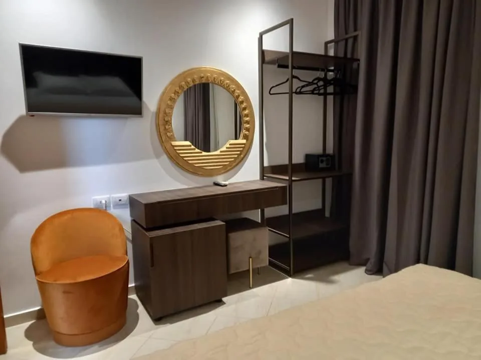 A desk with a round brass mirror, an orange velvet chair and an open metal wardrobe