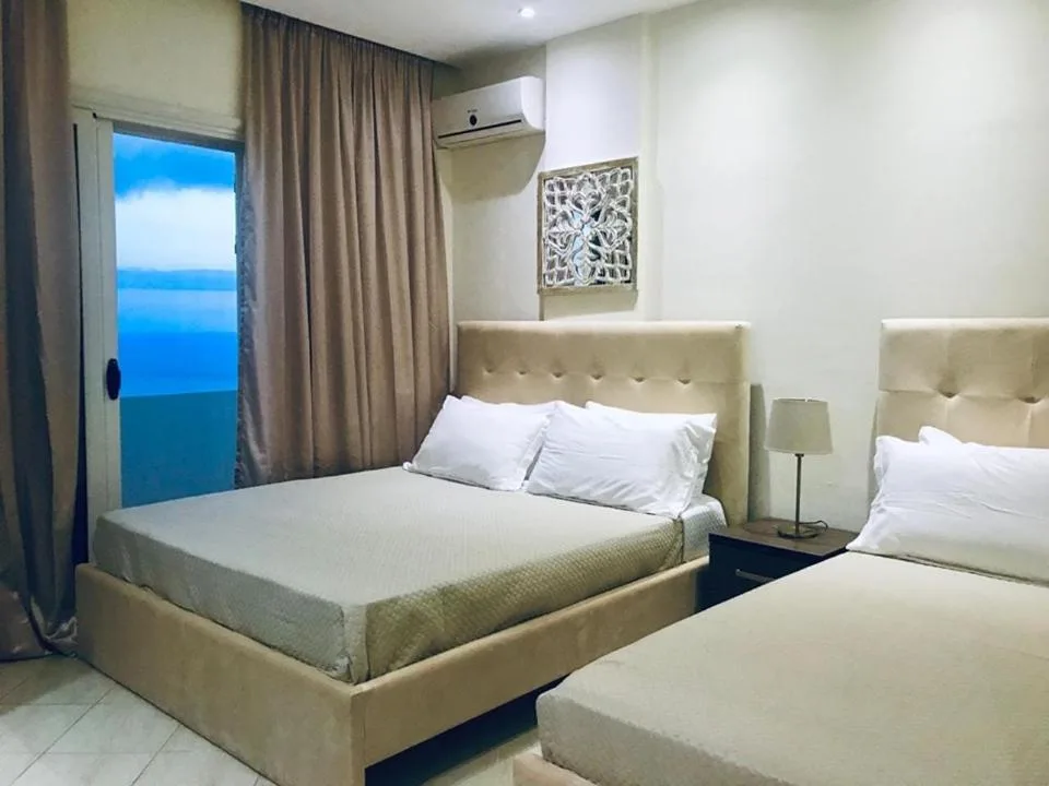 A double and a single bed with cream padded headboards, the balcony door open to the blue sea