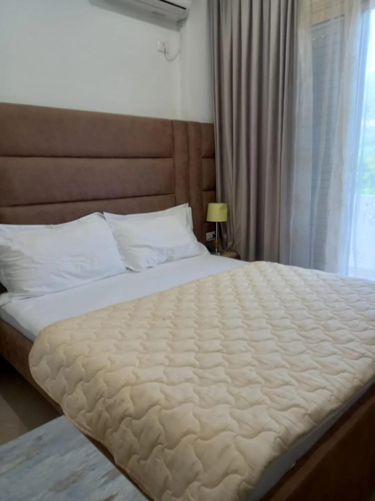 A compact double room with a brown headboard, a cream quilted bedspread and a bedside lamp