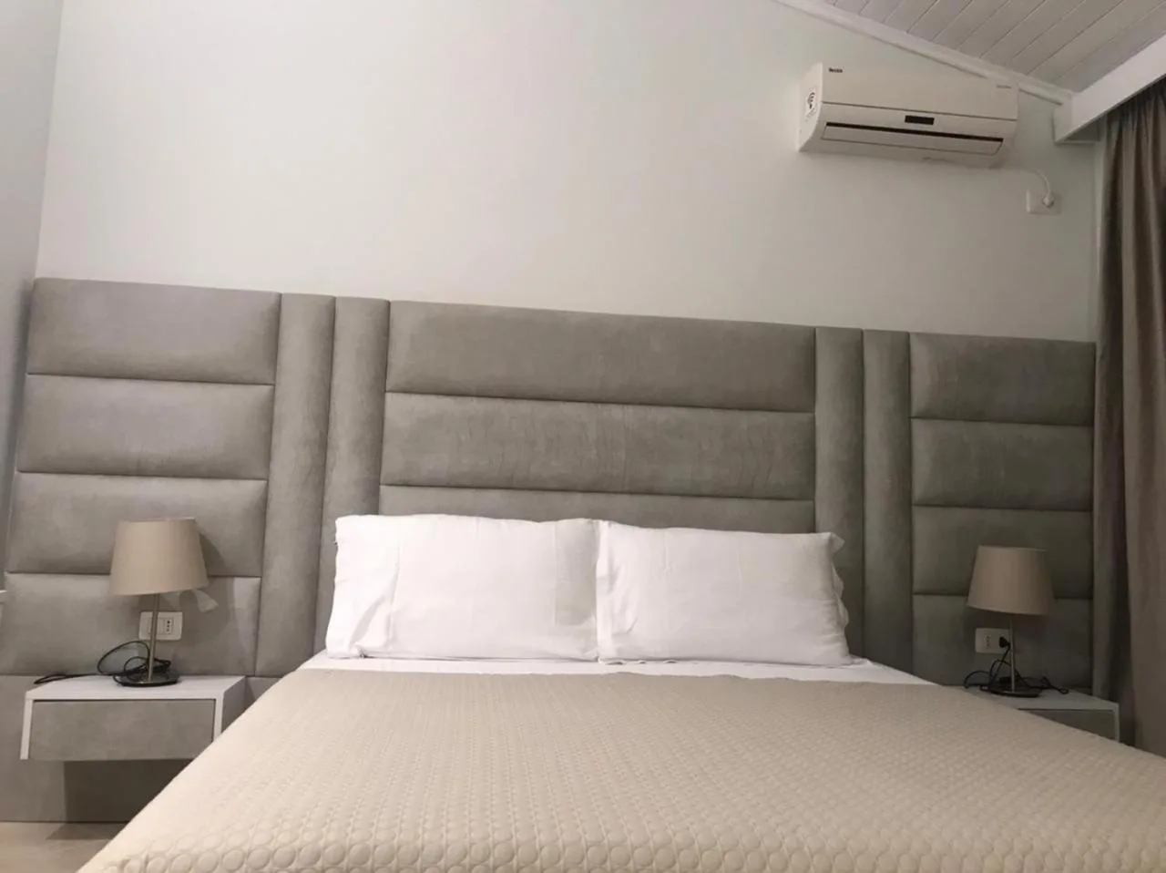 A double bed with a grey channelled headboard and two lamps on white floating bedside shelves