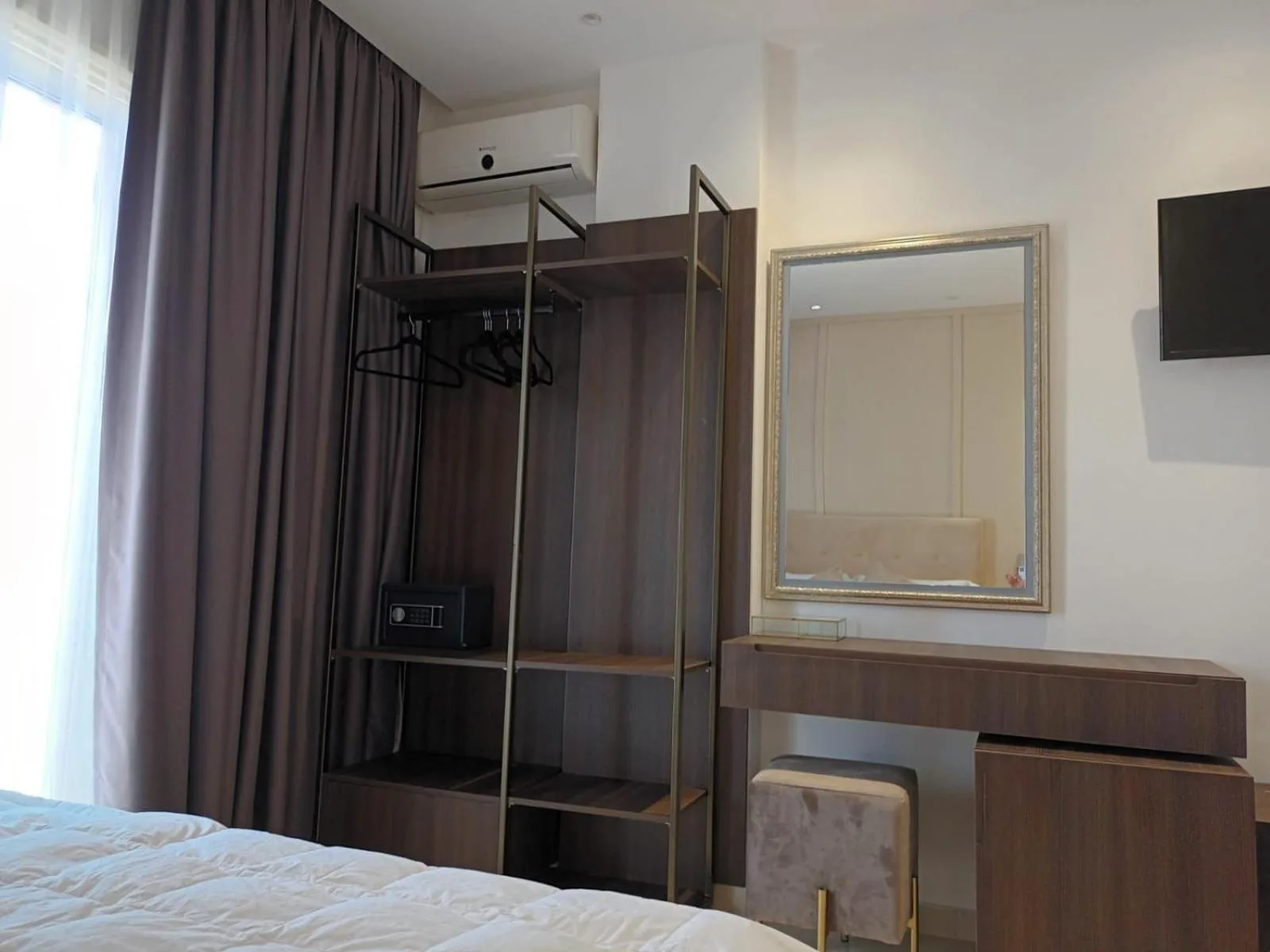 A wardrobe rail, a silver-framed mirror over a dressing table and a wall-mounted TV beside the bed