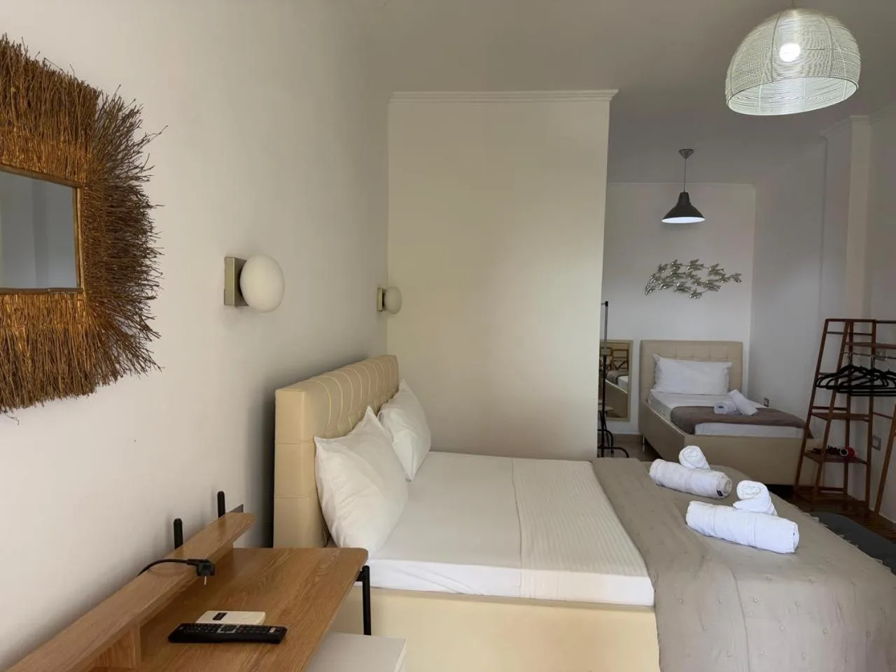A bright triple room with a straw sunburst mirror, a double bed, a single bed beyond and a rattan pendant lamp