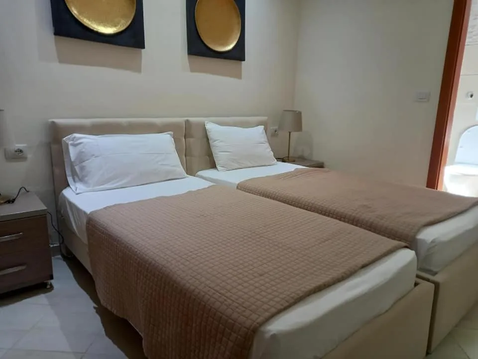 Two single beds with cream padded headboards and tan quilted covers under two gold disc wall pieces