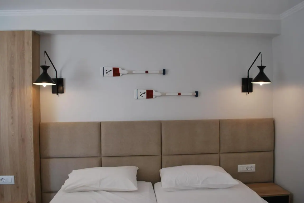 An upholstered headboard between two black wall lamps, with a framed painting beside it