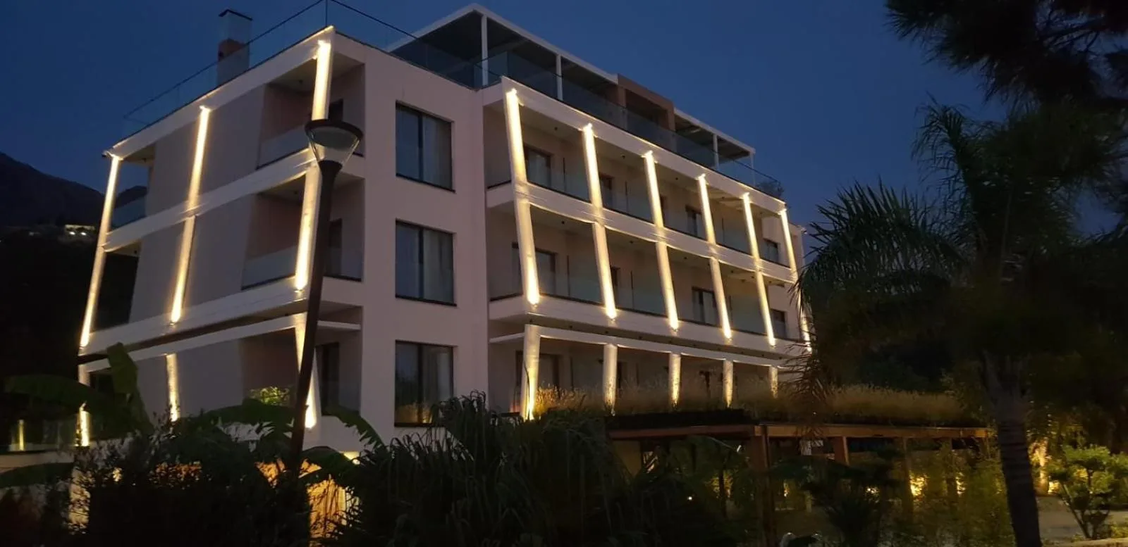 Light lines running up the balcony pilasters of the hotel at dusk, with palms in front