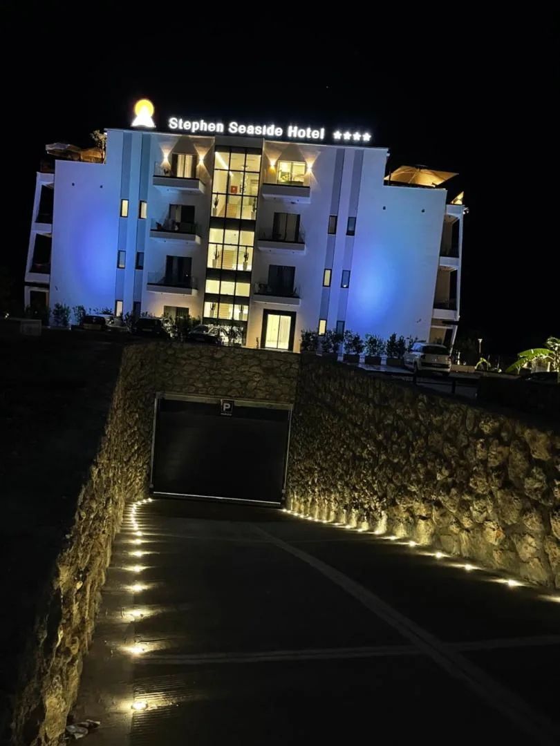 The hotel at night, its facade washed in blue light under the lit Stephen Seaside Hotel sign, above the stone-walled garage ramp