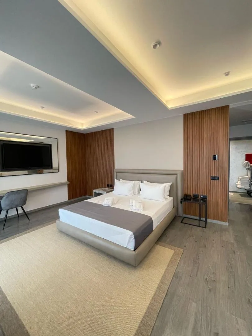 A room with a coved, lit ceiling, oak-slat panels either side of the bed, a jute rug and a desk