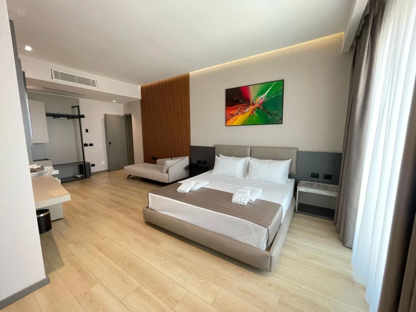 A double bed under an abstract painting, with an oak-slat panel and a dressing area behind
