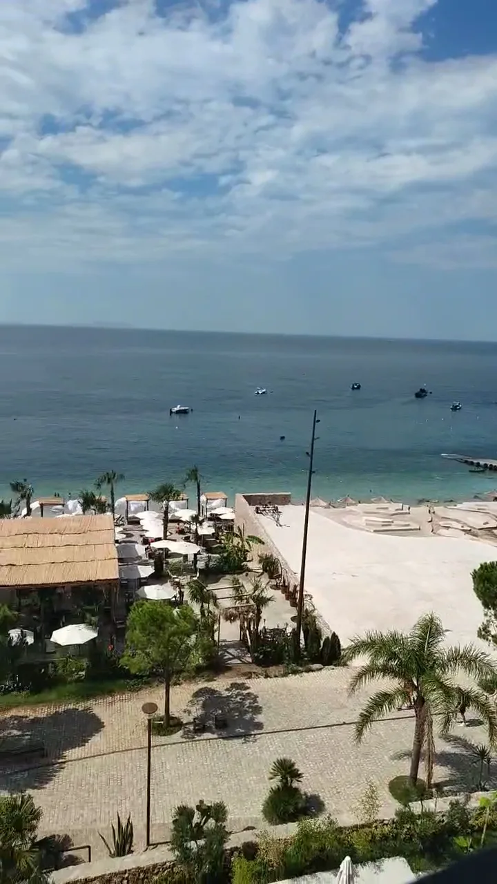 Looking down from an upper floor over the promenade, the thatched beach bar and the umbrellas to the open sea