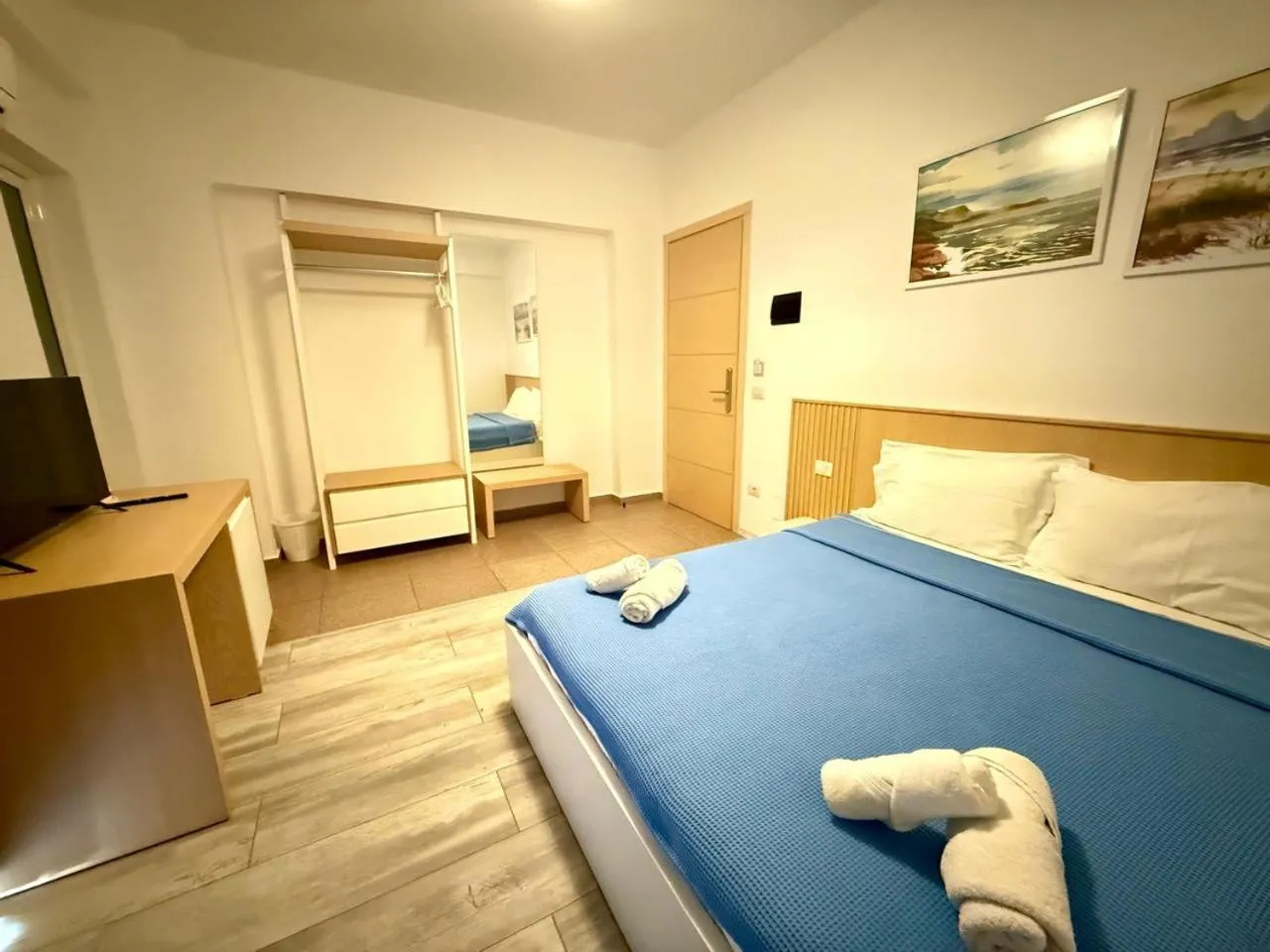 A double bed with towels folded on a blue cover, an oak headboard and two coastal paintings above