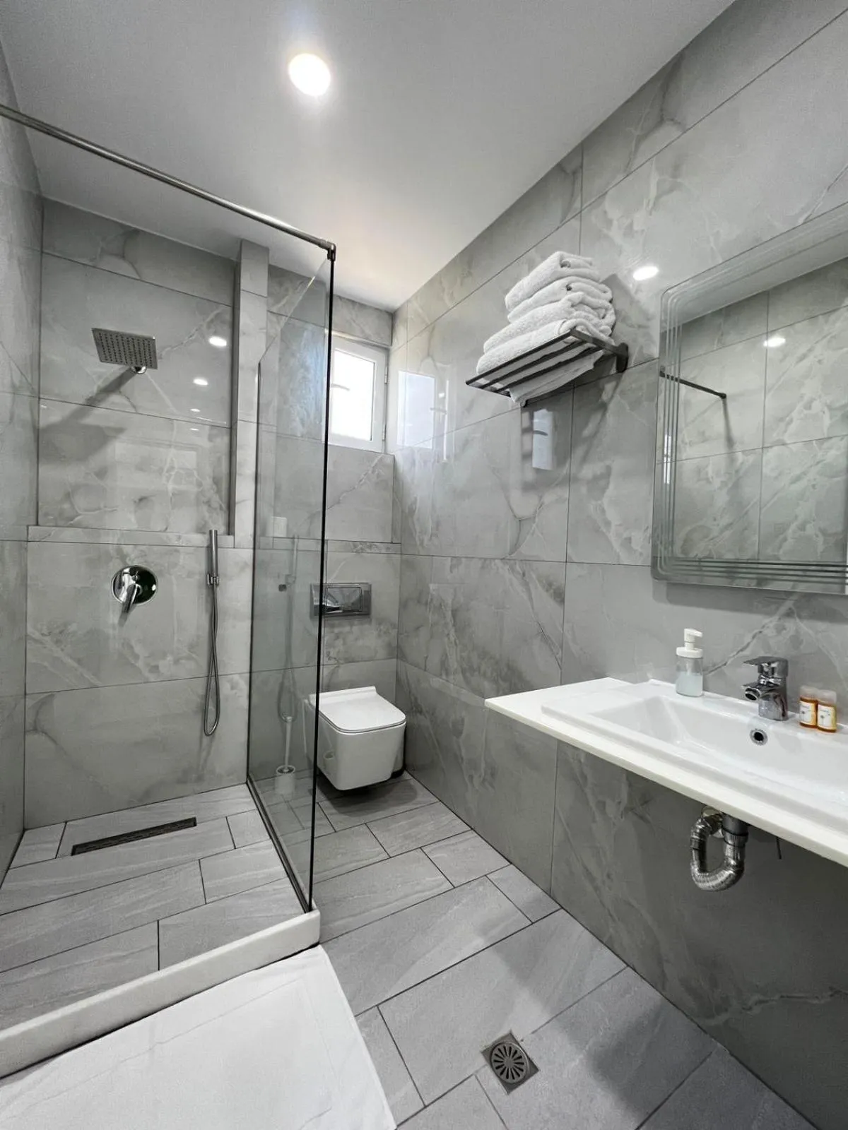 A shower room in grey marble-effect tile with a glass shower, a wall-hung toilet and a white basin