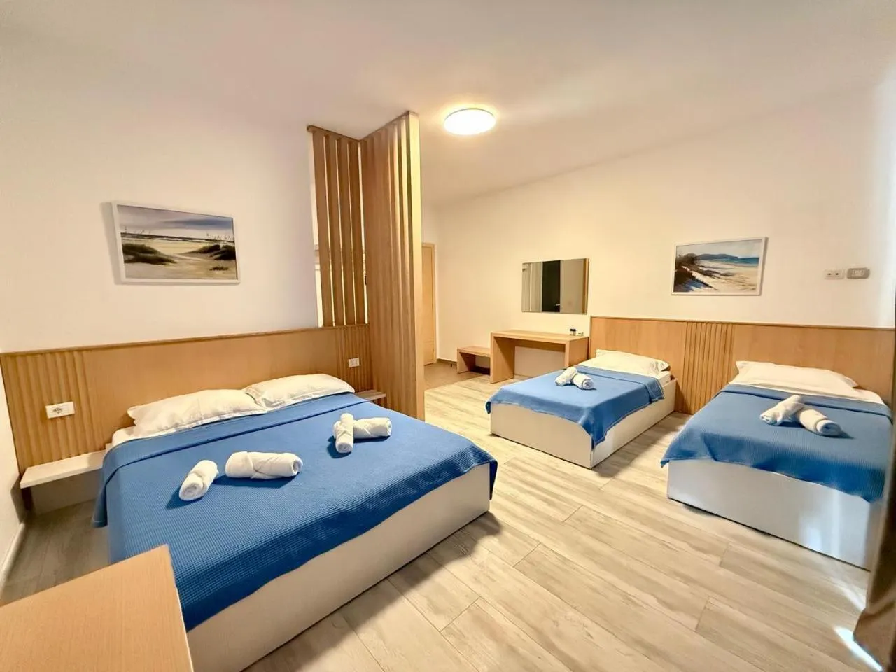 A double bed and two single beds with blue covers, an oak slatted screen and wall panelling, two beach paintings