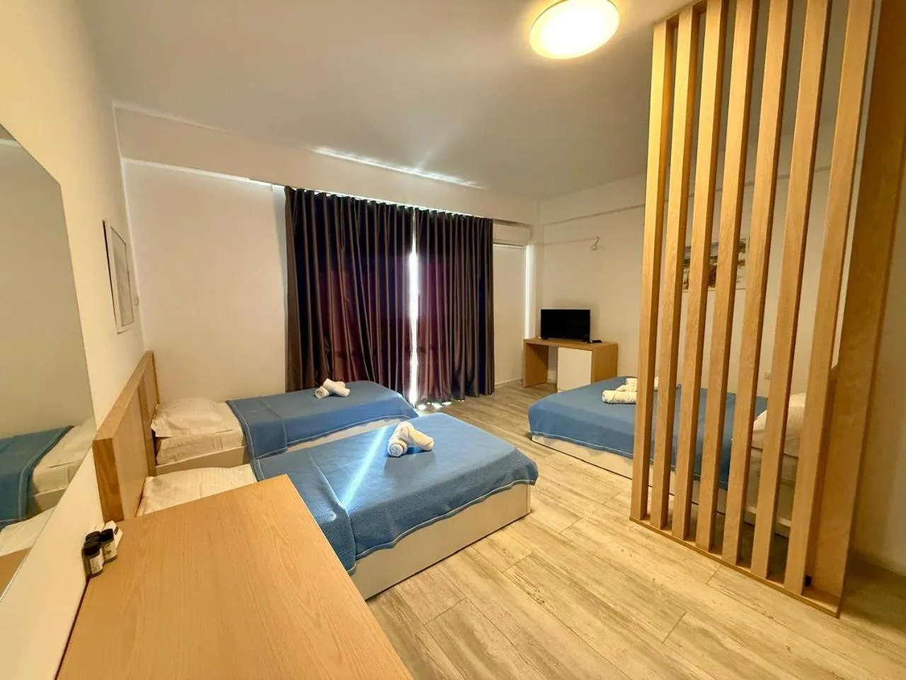 Beds with blue covers beside an oak slatted partition, dark curtains drawn across the balcony door
