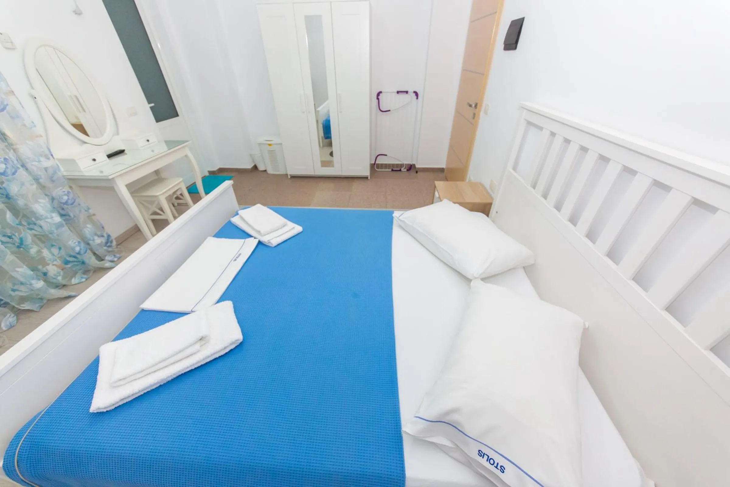 A white-framed double bed with a blue cover and a dressing table with an oval mirror
