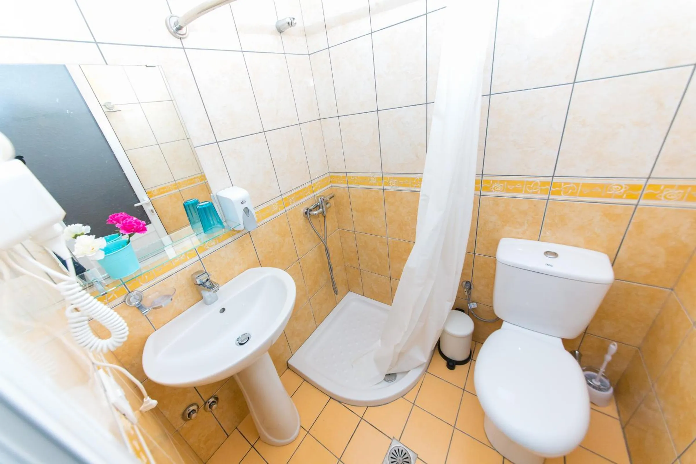 A tiled shower room with a basin, a toilet, a hairdryer and a shower curtain