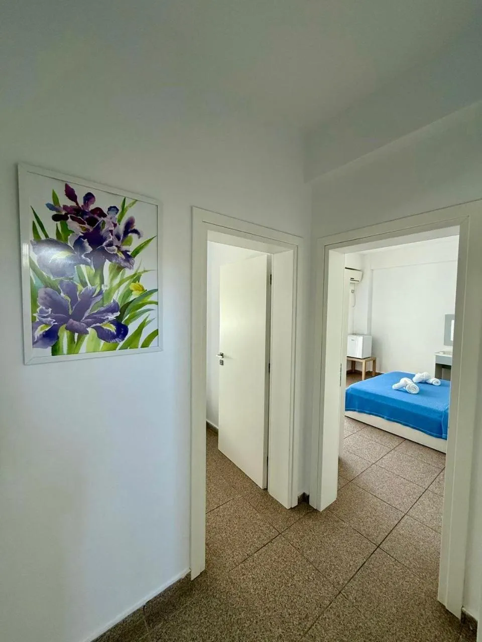 A painted purple iris on the wall, two doors open on a white corridor and a bed beyond