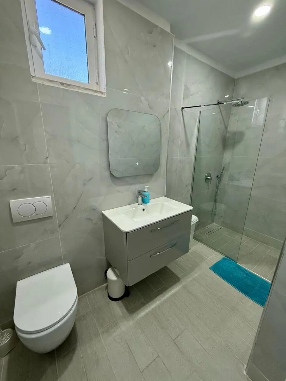 A shower room in grey marble-effect tile with a glass shower and a white vanity unit