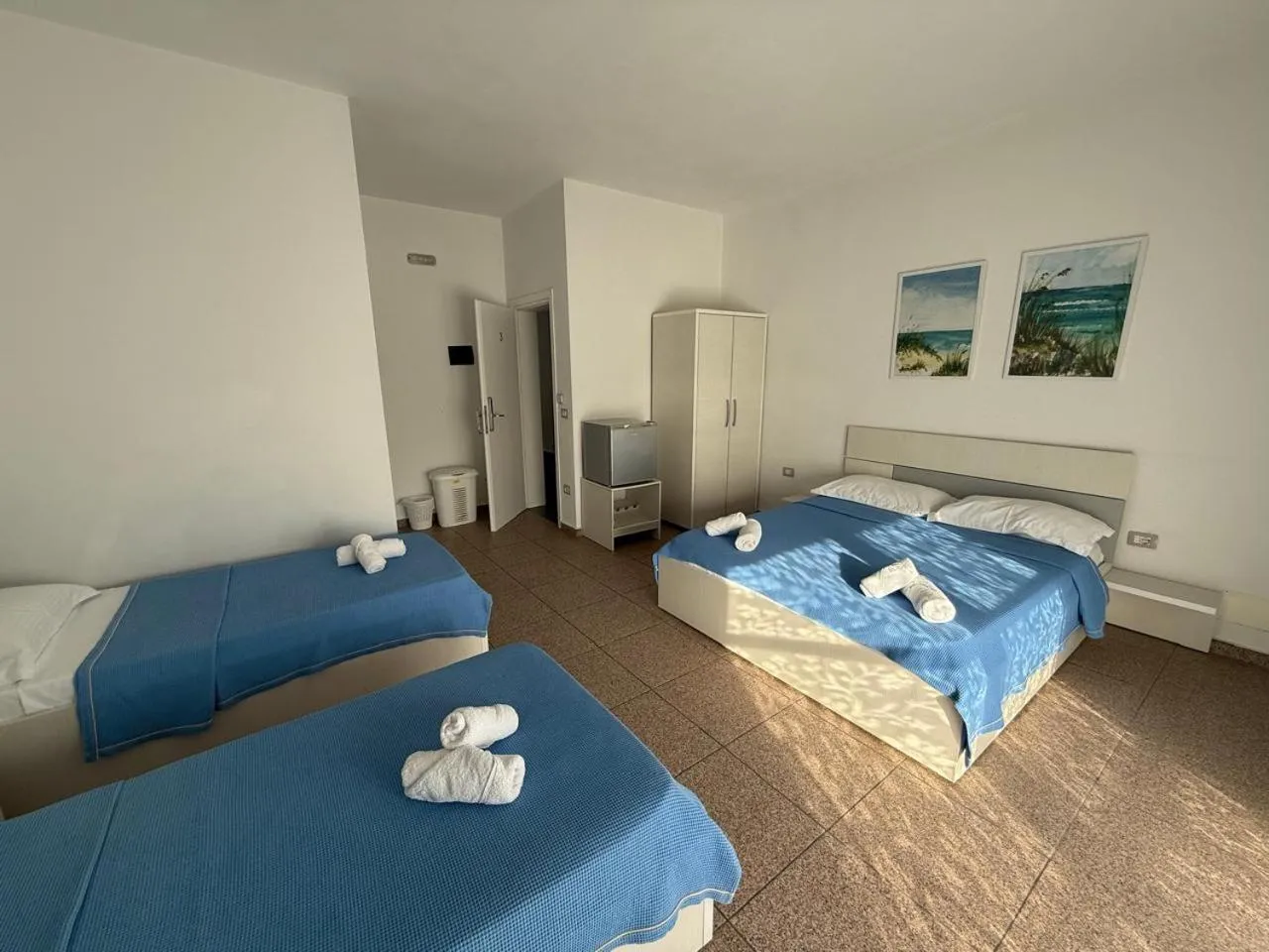 Two single beds and a double bed with rolled towels, two beach paintings on the wall