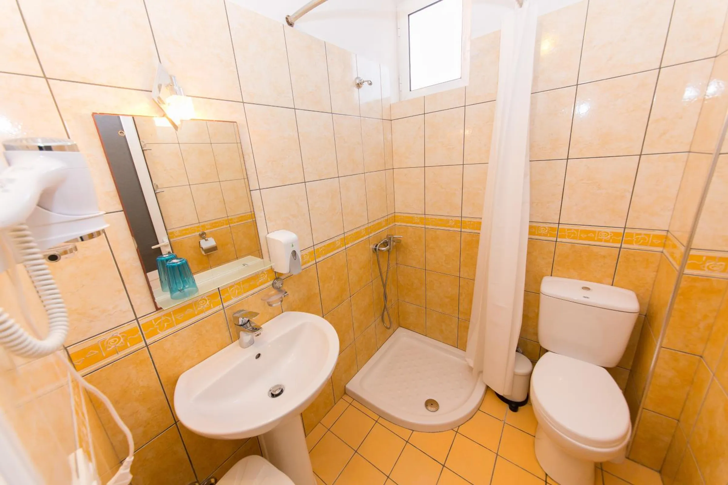 A tiled shower room with a basin, a mirror, a hairdryer and a shower cubicle