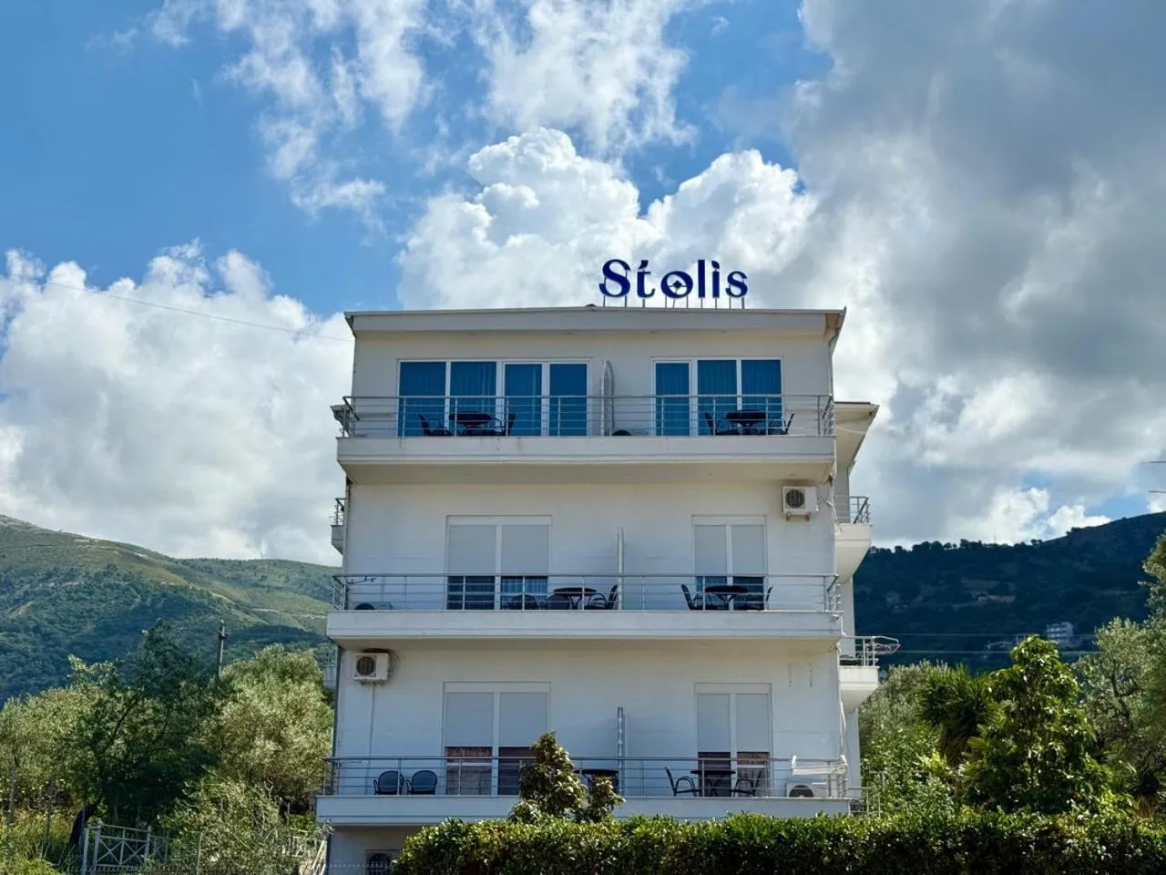 The four-storey white block of Hotel Stolis with balconies on every floor and the blue Stolis sign on the roof, green hills behind